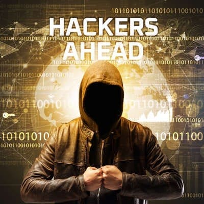 A faceless man in a hoodie stands with his fists together and the screen behind him reads "hackers ahead."